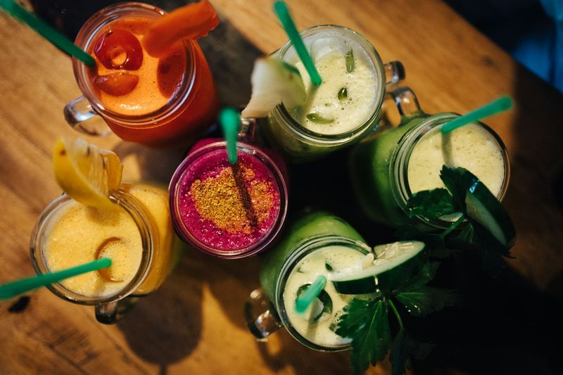 Seks fargerike juicer i glasskrus sett rett ovenfra på et trebord