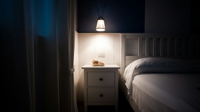 Tent nattbordslampe ved siden av en oppredd seng i et mørkt soverom