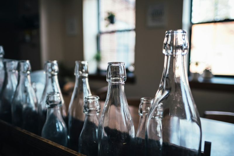 Flere klare glassflasker med kapsel står tett i rekke på et bord