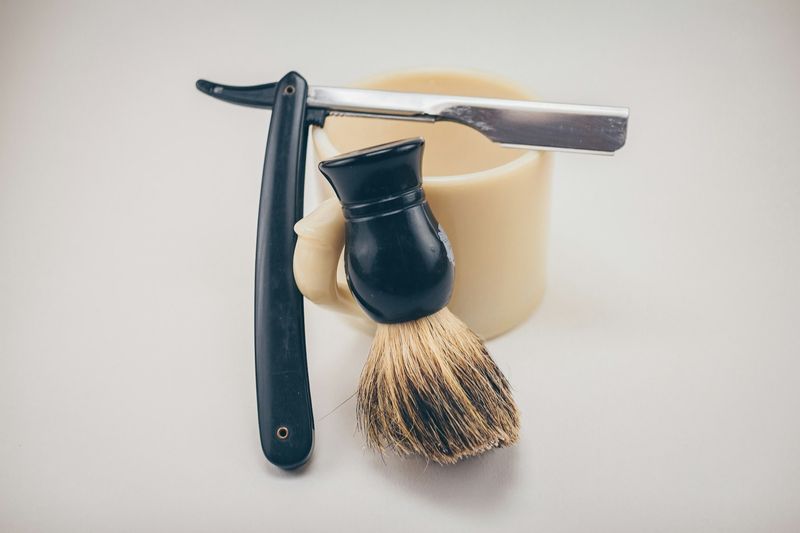 Gammeldags barberhøvel og barberkost lent mot en kremhvit kopp