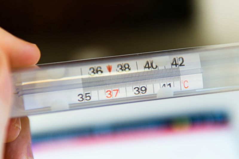 Et termometer med rød temperaturviser holdes opp mot lys bakgrunn