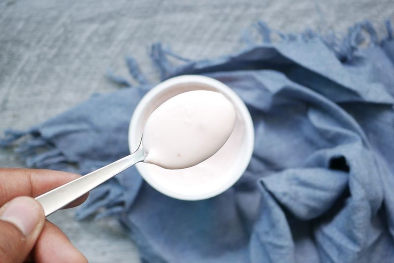 En hånd holder en skje med yoghurt over en skål
