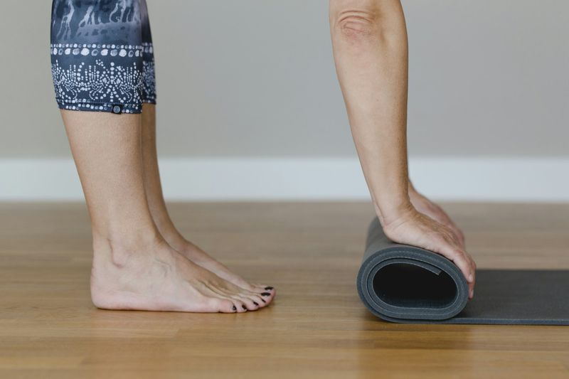 Bare føtter ved siden av en sammenrullet mørk yogamatte på tregulv