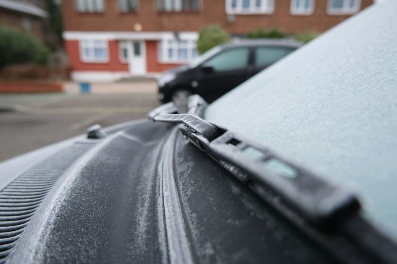 Rim og frost dekker frontruten og panseret på en parkert bil en kald morgen