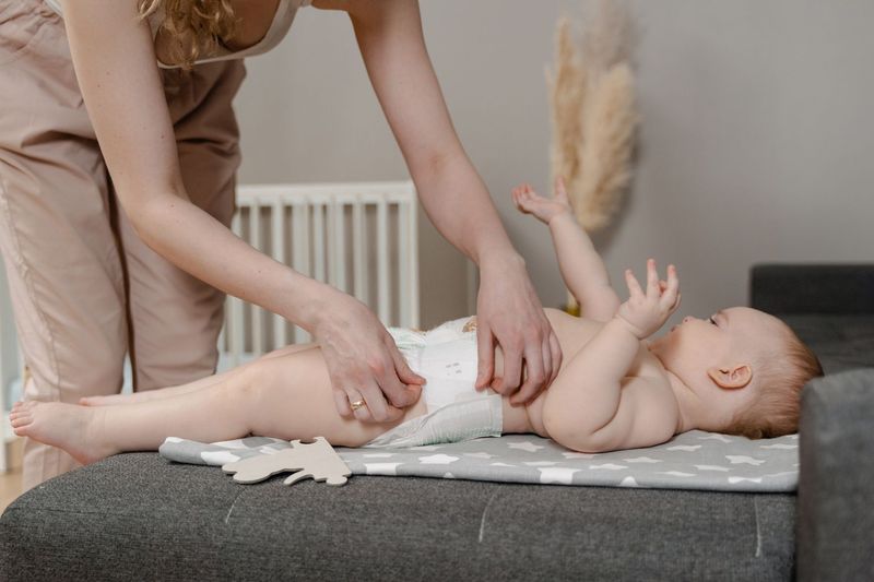 Mor skifter bleie på en baby som strekker armene i været