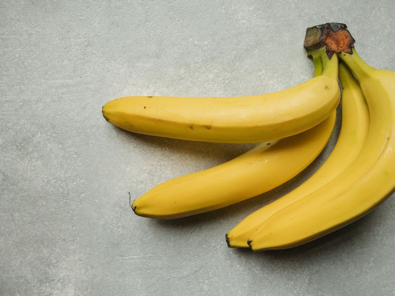 Gule bananer i en klase på en grå steinbenk i dagslys