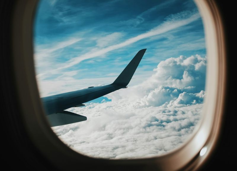 Utsikt gjennom et rundt flyvindu mot vingen og hvite skyer