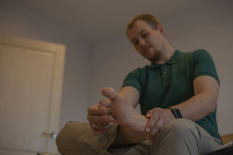 En mann sitter på sengekanten og undersøker sin egen fot