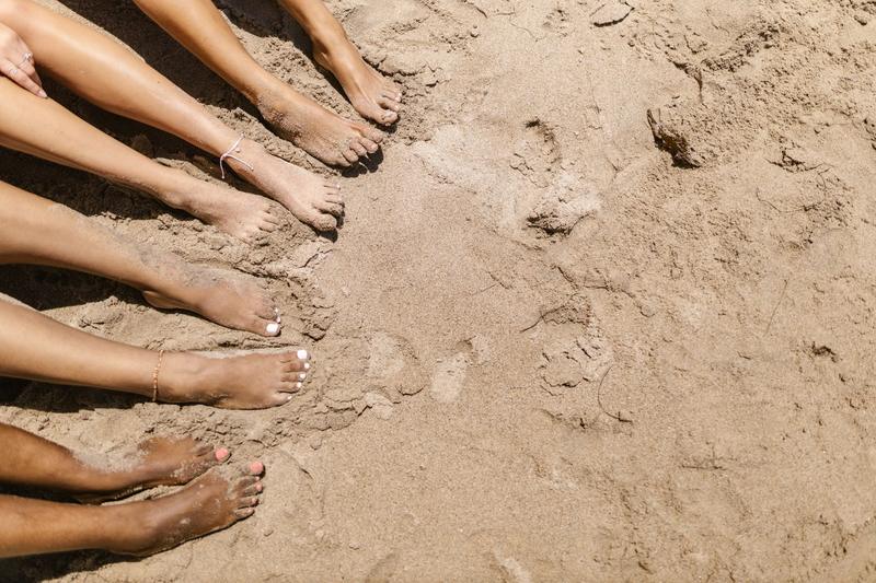 Flere bare føtter med lakkerte tær på lys sand ved stranden