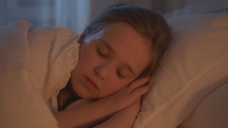 Ung jente sover fredelig med hodet på armen i varmt lys
