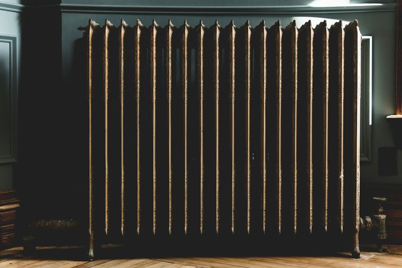 Gammel støpejernsradiator mot en mørk vegg i lavt sidelys
