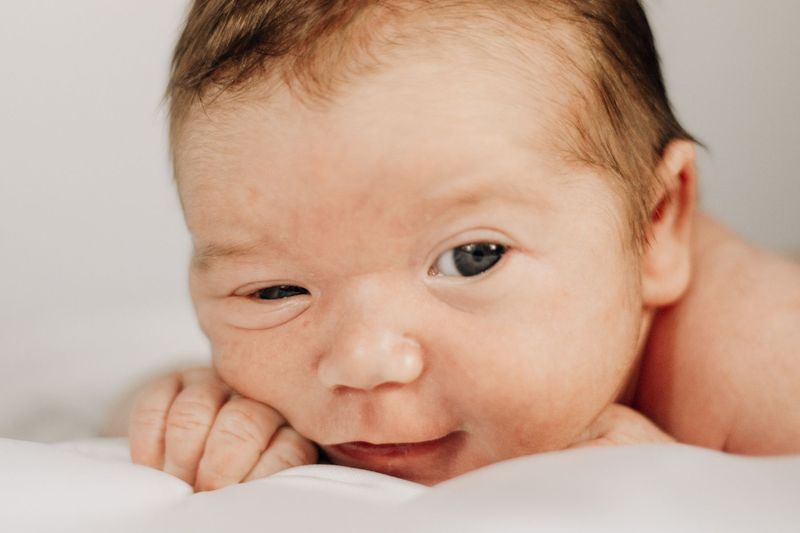 Nyfødt baby med åpne øyne hviler kinnet mot en hvit pute