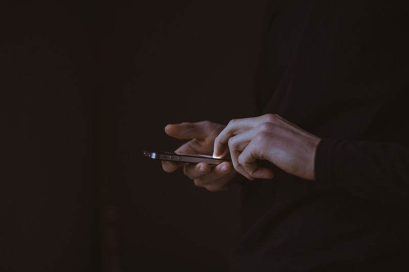 To hender skriver på en mobiltelefon i et mørkt rom