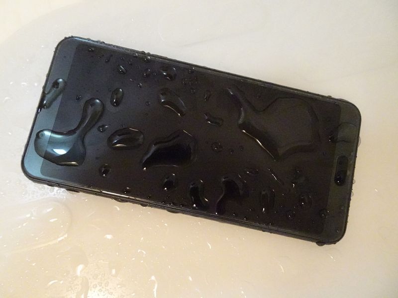 Svart smarttelefon dekket av vanndråper på en lys benkeplate